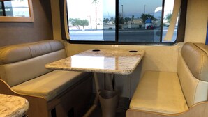 A compact RV interior with a small kitchenette, seating area, and a window providing a view of the outside. - Road Surfer-- Resort-Style RV Stay Near The Strip (Las Vegas)