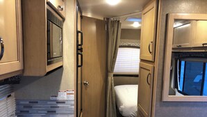A compact RV interior with a kitchenette, a bed, and a small bathroom. - Road Surfer-- Resort-Style RV Stay Near The Strip (Las Vegas)