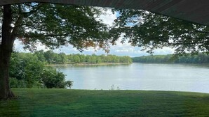 Une vue sur un lac, prise depuis un espace abrité, avec un pré verdoyant au premier plan et des arbres en arrière-plan.