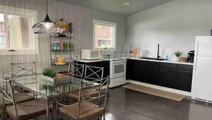 Une cuisine moderne avec une table à manger en verre, des meubles de rangement noirs, des appareils électroménagers blancs et un luminaire suspendu.
