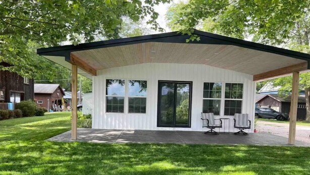 Un espace extérieur abrité, doté d’un toit en bois et de grandes fenêtres, et entouré d’une pelouse bien entretenue.