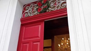 A red door with a decorative wreath and a chandelier visible inside.