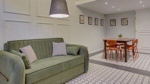 A green sofa with patterned pillows, a dining table with chairs, and a ceiling light fixture.