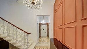 A hallway with a staircase, a chandelier, and a door at the end.