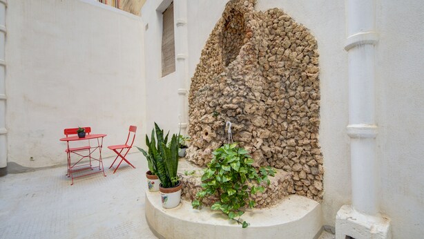 A courtyard with a stone wall, a small table with a chair, and potted plants.