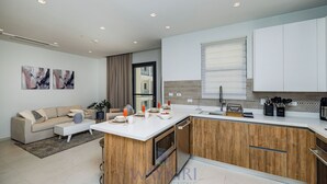 A modern kitchen with wooden cabinets, a white countertop, and a built-in oven. There is a dining area with a sofa and a coffee table. - Wariruri 2-13 BRAND NEW Apartment, private balcony! (Noord)