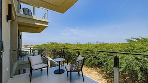 A balcony with a glass balustrade, two chairs, a small round table, and a view of green vegetation. - Wariruri 2-13 BRAND NEW Apartment, private balcony! (Noord)