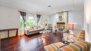 A spacious living room with a sofa, armchairs, a glass coffee table, and a fireplace with a stone wall. - Upper East Side - Miami Home - We Host (Miami)