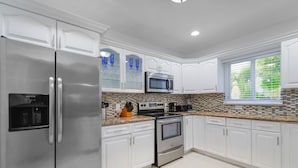 A modern kitchen with white cabinets, stainless steel appliances, and a tiled backsplash. - Upper East Side - Miami Home - We Host (Miami)