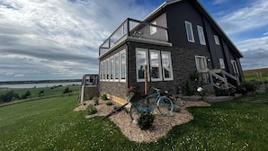 A two-story house with a balcony, large windows, and a view of a lake.