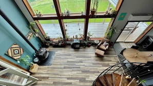A spacious living area with a large window overlooking a green landscape, a wooden staircase, and a cozy seating area.