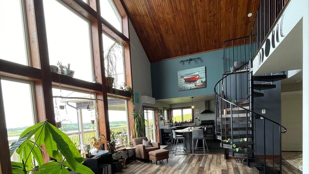 A spacious interior with large windows, a wooden ceiling, a modern kitchen, and a spiral staircase.