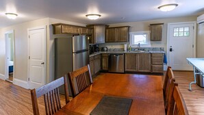 A modern kitchen with wooden cabinets, stainless steel appliances, and a dining area with a wooden table and chairs. - Spacious 2 bedroom historic home with two king beds and kitchenette. (Ashland)