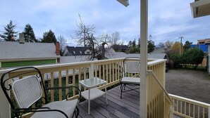 A wooden deck with two wicker chairs and a small table, overlooking a residential area with houses and trees. - Spacious 2 bedroom historic home with two king beds and kitchenette. (Ashland)