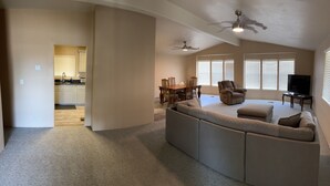 A spacious living area with a large sectional sofa, a dining table with chairs, a ceiling fan, and a television. - Enjoy living on a pecan orchard surrounded by trees!!!!!!
 (Las Cruces)