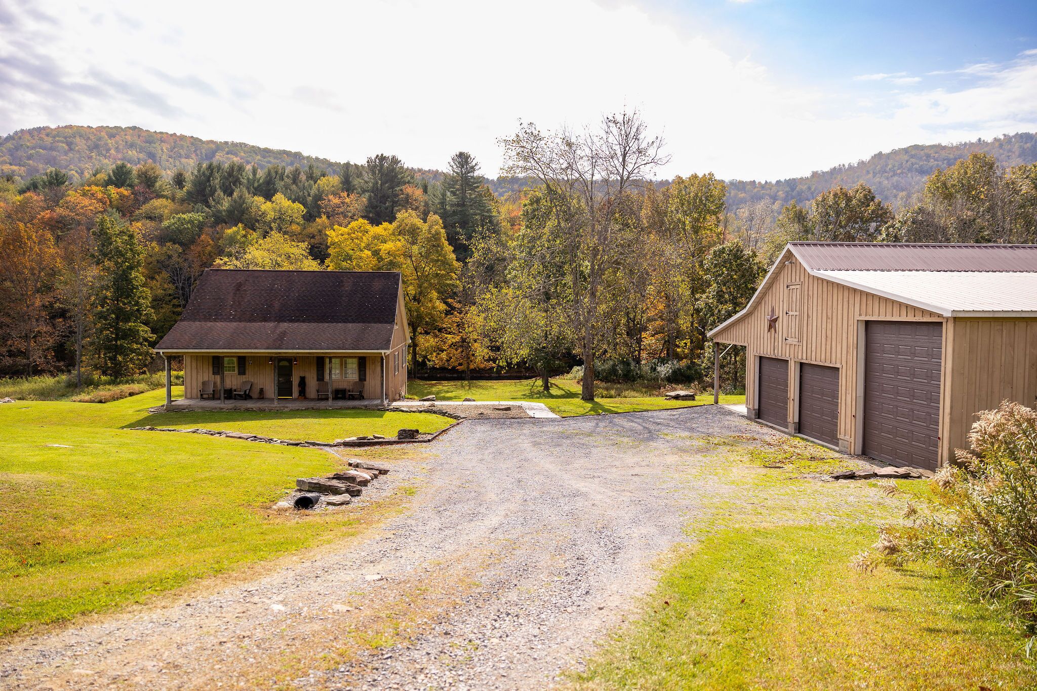 A rural property with a gravel driveway, a wooden house, and a barn.