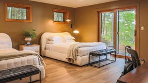 A bedroom with a bed, a bench, a chair, a table, and a sliding glass door leading to a balcony. - TC Lake House w/Hot Tub, Pontoon, & Game Room! (Traverse City)