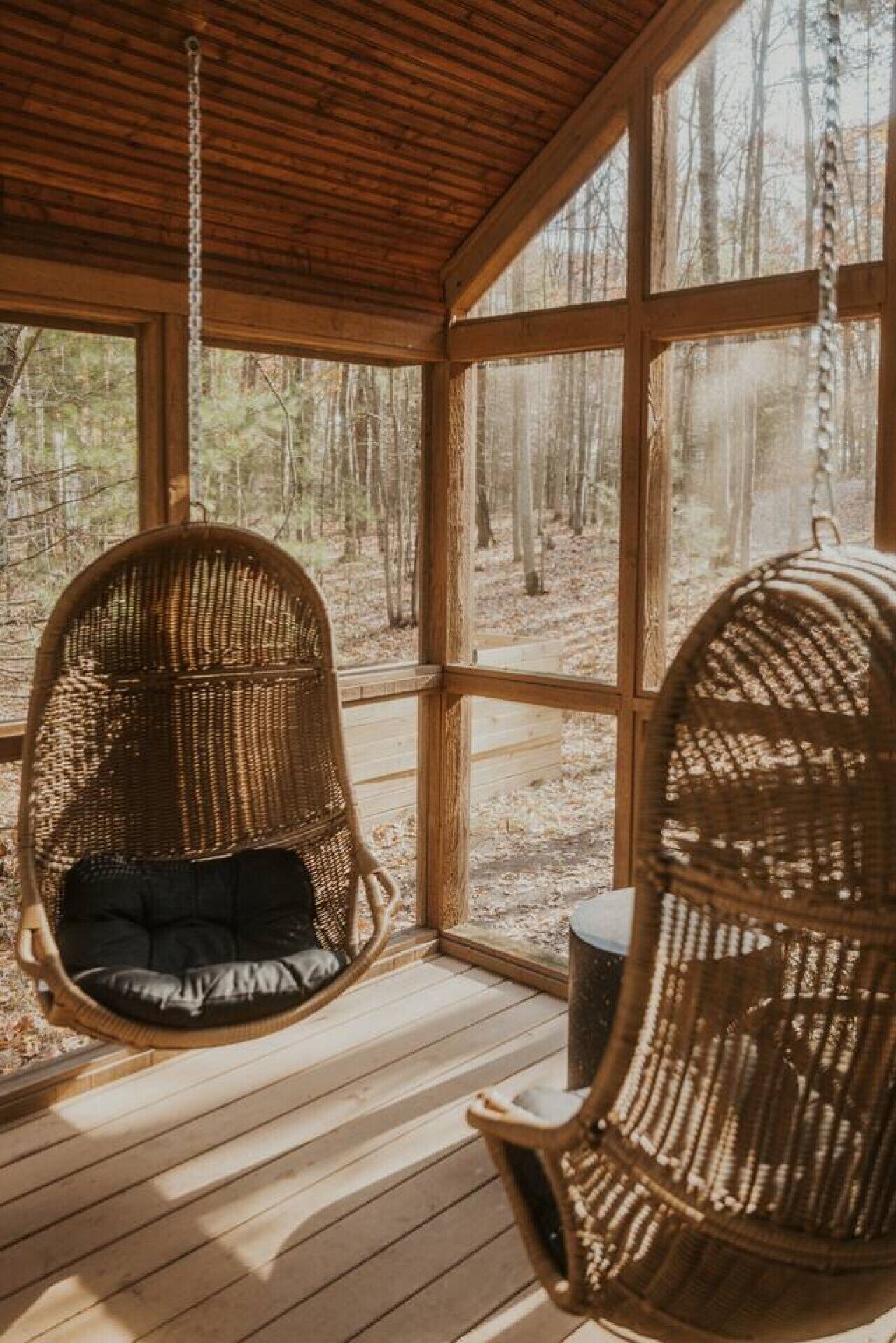 A wooden cabin with a porch, two wicker chairs, and a view of a forest.