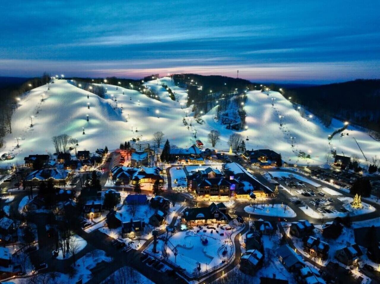A snow-covered town with illuminated buildings and a ski slope.