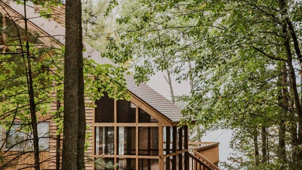 A wooden cabin with a deck, surrounded by trees. - TC Lake House w/Hot Tub, Pontoon, & Game Room! (Traverse City)