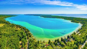 A coastal landscape with a large body of water, dense greenery, and a few buildings along the shore. - TC Lake House w/Hot Tub, Pontoon, & Game Room! (Traverse City)