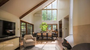 A modern living room with a TV, fireplace, dining area, and large windows. - TC Lake House w/Hot Tub, Pontoon, & Game Room! (Traverse City)