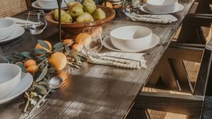 Een eettafel gedekt met borden, kommen, glazen en een middelpuntstuk met gedroogde takken en fruit.
