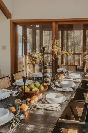 Una mesa de comedor dispuesta con platos, tazones, vasos y un centro de mesa con ramas secas y frutas.