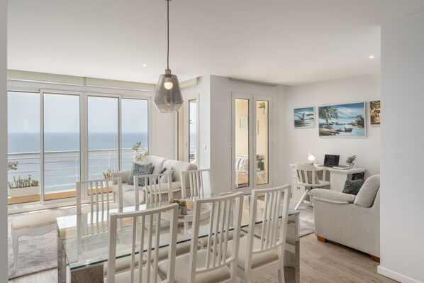 Enjoy a sea view from the large window in this stylish living space, featuring a glass dining table, comfortable sofa, and desk.