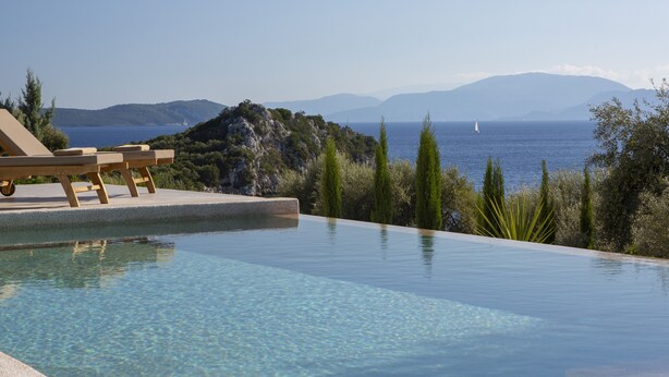 An infinity pool with clear blue water, wooden lounge chairs, and a view of the sea and mountains. - Sea View Villa Selina with private sea access and infinity pool (Sivota Lefkada)