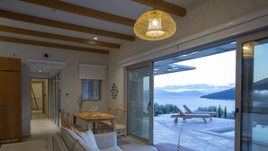 A modern living room with a sofa, dining table, and chairs, a large window with a view of the sea, and a hanging light fixture. - Sea View Villa Selina with private sea access and infinity pool (Sivota Lefkada)