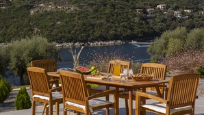 Mesa de madera al aire libre con sillas, vista a un lago y una ladera boscosa al fondo.