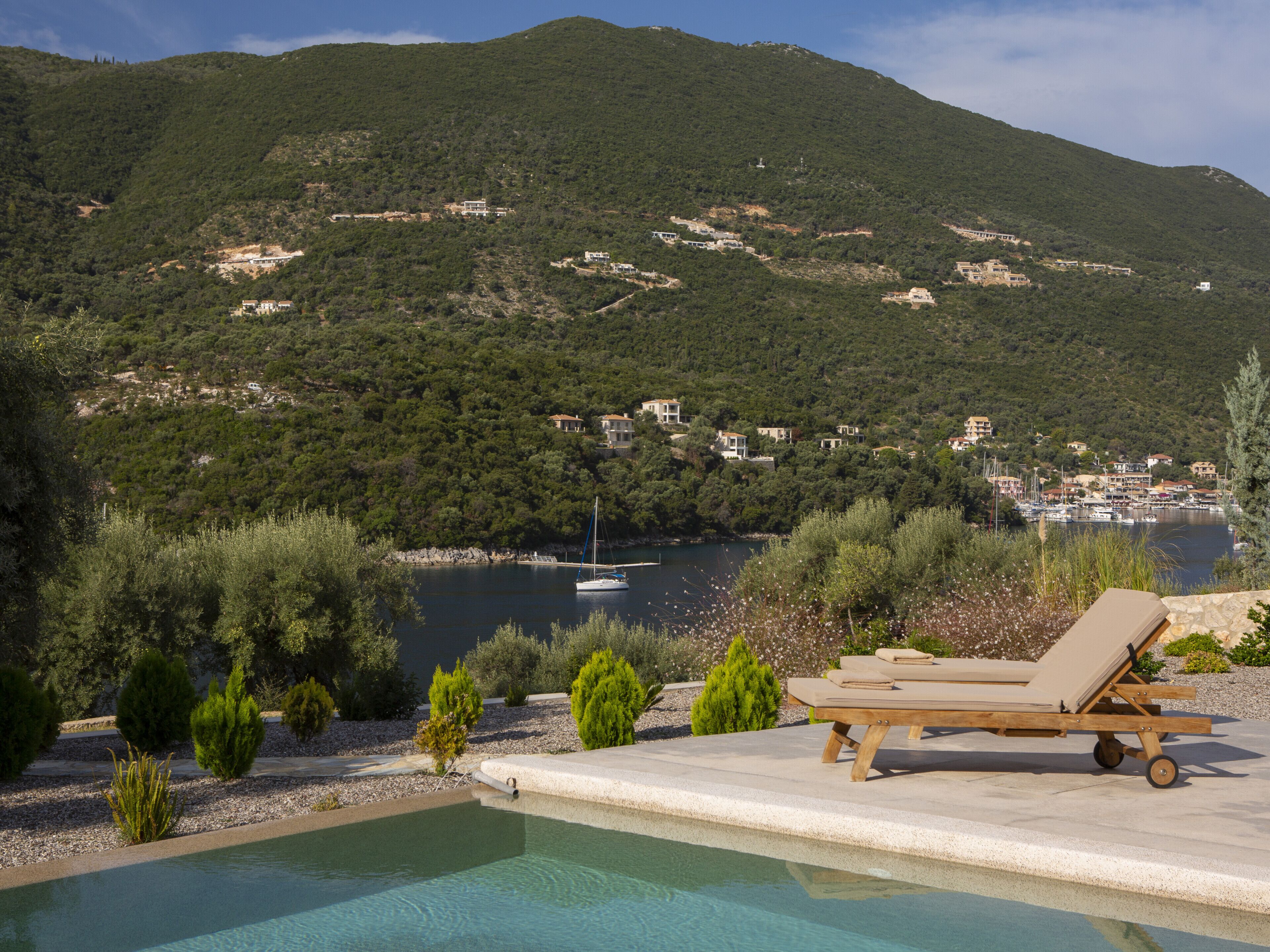 A pool with lounge chairs, a view of a lake, and buildings on a hillside.