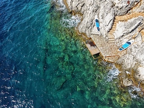 Zona costera con agua cristalina, terreno rocoso y una estructura de madera con un objeto azul y blanco en la parte superior.