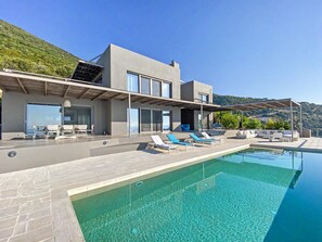 A modern house with a swimming pool, outdoor seating, and a view of the hills.