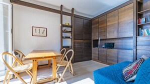 A modern living room with a wooden table and chairs, a blue sofa with a patterned cushion, and a built-in bookshelf with books and decorative items. - Apartment in Recco with 1 bedrooms sleeps 4 (Recco)