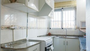 Eine Küche mit weißen Schränken, einer Granit-Arbeitsplatte, einem Herd, einer Spüle und einem Fenster mit Jalousien.