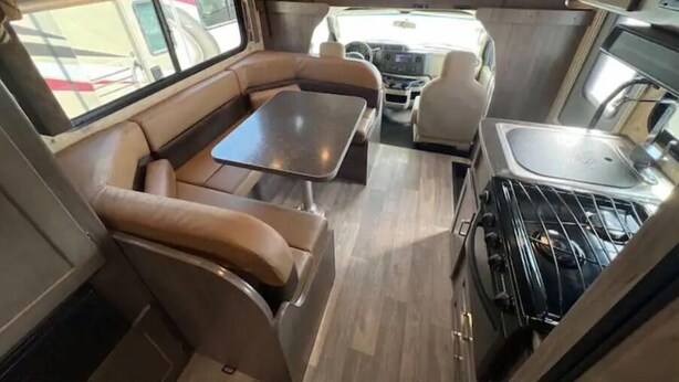 Ein kompaktes Wohnmobil-Interieur mit Essbereich, einer Küchenzeile und einer Sitzecke mit Tisch und Stühlen.