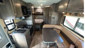 Ein kompaktes Wohnmobil-Interieur mit einer Küchenzeile, einem Esstisch und einer Sitzecke.