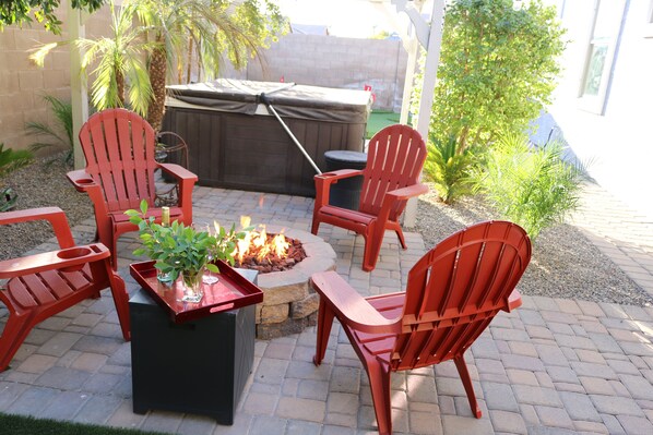 Une terrasse extérieure avec des fauteuils Adirondack rouges, un foyer et un barbecue couvert.