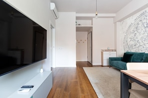A modern living room with a flat-screen TV, a wooden floor, a green sofa, and a desk with a chair.