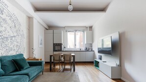 A modern living room with a sofa, a dining table, chairs, a kitchen area with cabinets, a TV, and a map on the wall. - GuestHost - Modern and welcoming 80m2 apartment, ideal for 4 people, located on the mezzanine floor of a building (NO lift) in the Bullona area. The property is located in a strategic area, a few minutes walk from the “Gerusalemme” and “Domodossola (Milano)