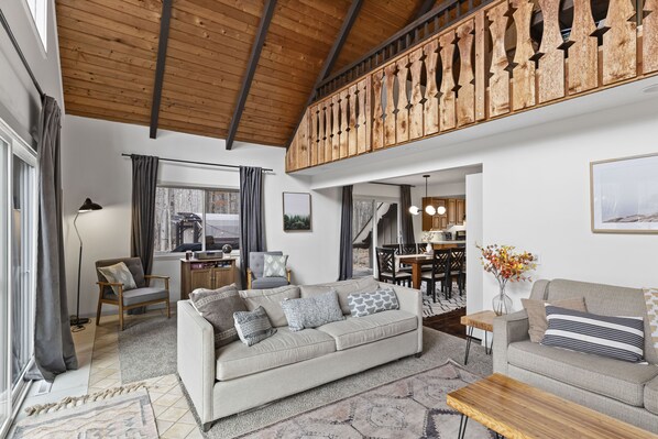 A spacious living area with a high wooden ceiling, a large sofa, a smaller sofa, and a wooden coffee table. - Rustic Chalet Retreat w/ Hot Tub (Stanwood)