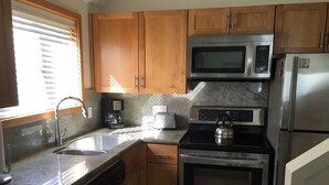 A kitchen with wooden cabinets, a stainless steel microwave, a coffee maker, a kettle, and a dishwasher. - Sealodge J7 - 2BR/2BA, 2nd Floor Prime End Unit, Spectacular Oceanfront Views (Princeville)