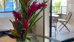 A room with a glass table, a vase with flowers, a view of the ocean, and a balcony with chairs. - Sealodge J7 - 2BR/2BA, 2nd Floor Prime End Unit, Spectacular Oceanfront Views (Princeville)