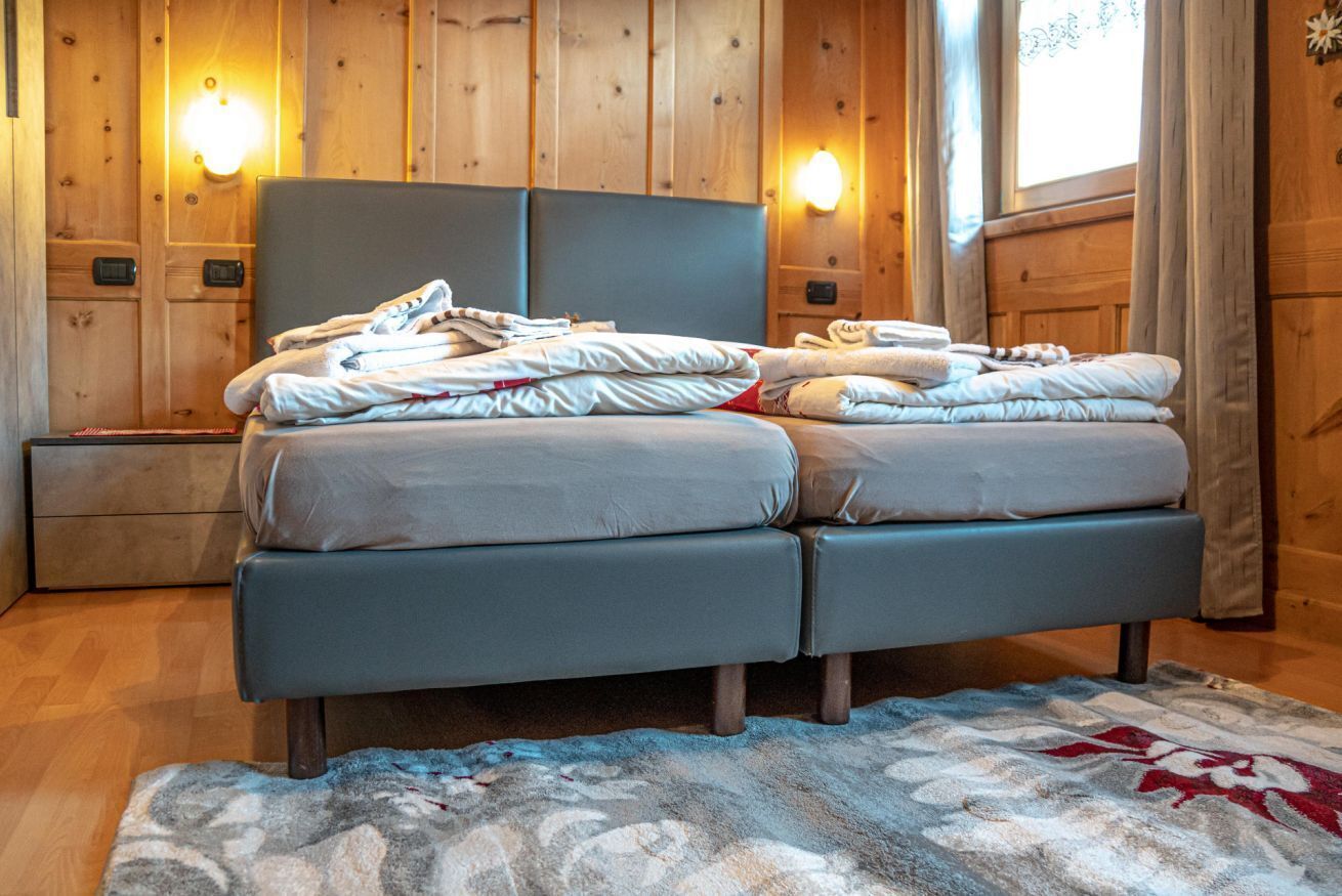 A double bed with a grey headboard, two bedside tables, and a wooden wall with built-in lighting.