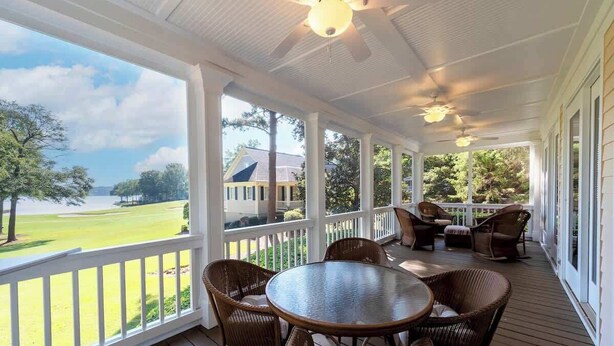 Une véranda aménagée avec des meubles en osier, une table ronde et une vue sur un terrain de golf et une maison.