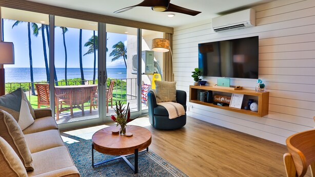A modern living room with a large TV, comfortable seating, and a view of the ocean.