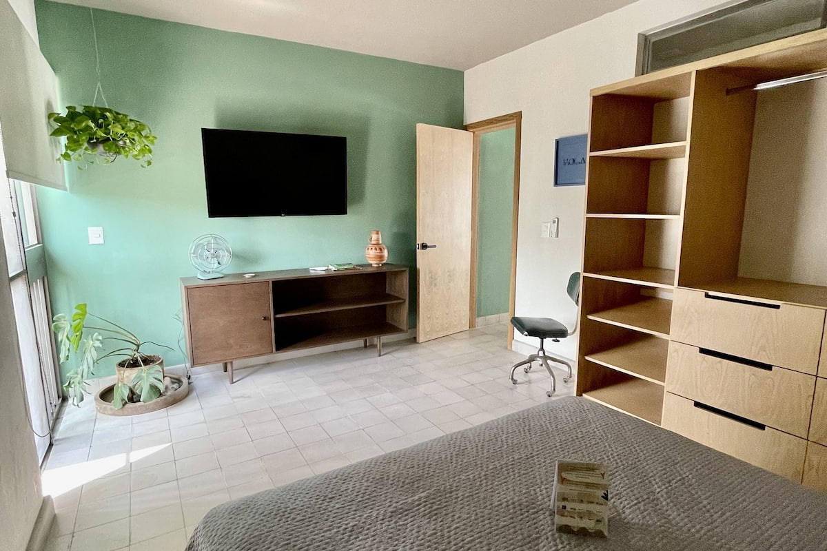 Een slaapkamer met een bed, een televisie, een houten garderobe, een bureau en een stoel.