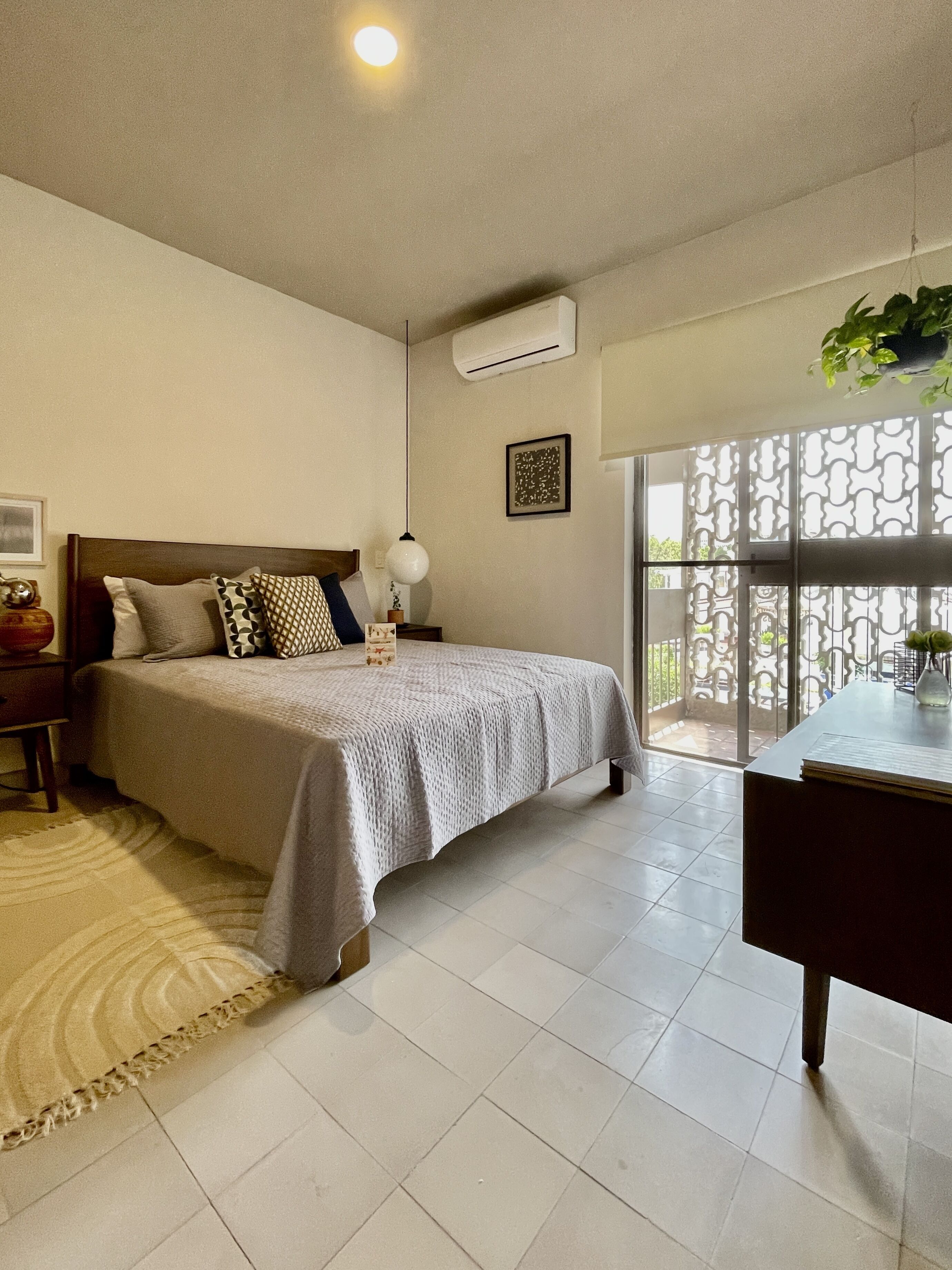 Un dormitorio con cama, mesita de noche, lámpara, aire acondicionado y vistas al exterior.